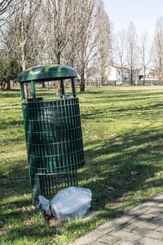 A lot of trash abandoned outside a waste basket in the park