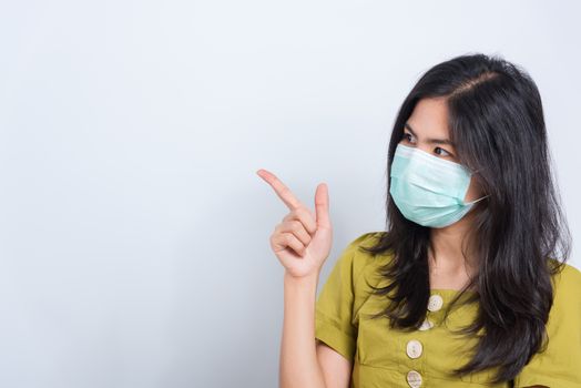 Portrait Asian beautiful happy young woman wearing face mask protects filter dust pm2.5 anti-pollution, anti-smog, and air pollution her pointing out to space on a white background, with copyspace
