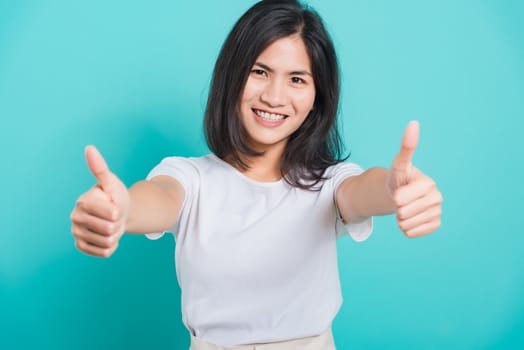 Portrait Asian beautiful young woman standing, She made finger thumbs up, Ok sign to agree and looking at camera, shoot photo in studio on blue background, There was copy space