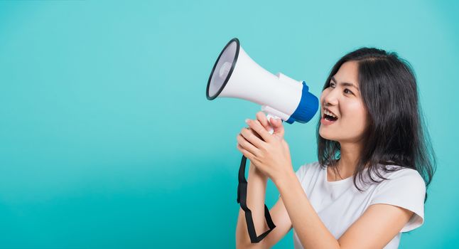 Portrait Asian beautiful young woman standing smile holding and shouting into megaphone looking to space, shoot the photo in a studio on a blue background, There was copy space