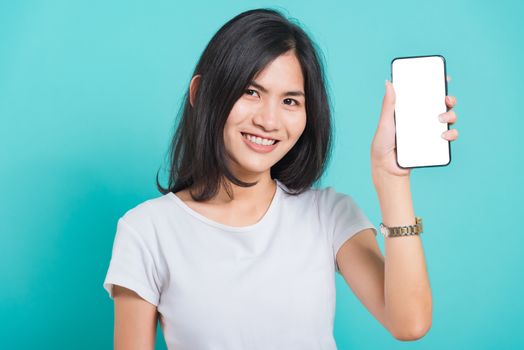 Portrait Asian beautiful happy young woman standing smile showing blank screen mobile phone looking to camera, shoot the photo in a studio on a blue background, There was copy space