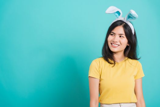 Portrait Asian beautiful happy young woman smile white teeth wear yellow t-shirt standing with bunny ears her looking to space, on blue background with copy space