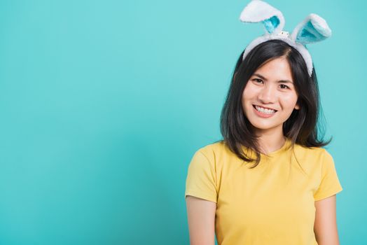 Portrait Asian beautiful happy young woman smile white teeth wear yellow t-shirt standing with bunny ears her looking to camera, on blue background with copy space