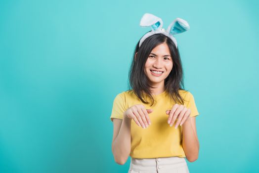 Portrait Asian beautiful happy young woman smile white teeth wear yellow t-shirt standing with bunny ears using hand to gesture rabbit her looking camera, on blue background with copy space
