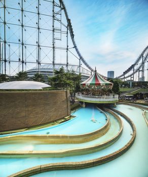 Laqua Tokyo Dome City Mall with its impressive roller coaster integrated in the gallery of its shopping center with a carousel  and water coaster under the summer blue sky.