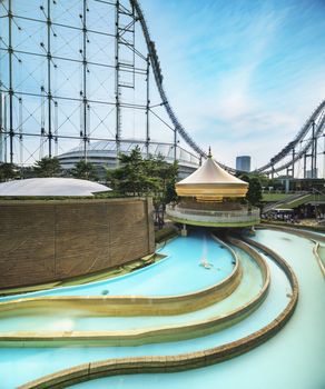 Laqua Tokyo Dome City Mall with its impressive roller coaster integrated in the gallery of its shopping center with a carousel  and water coaster under the summer blue sky.