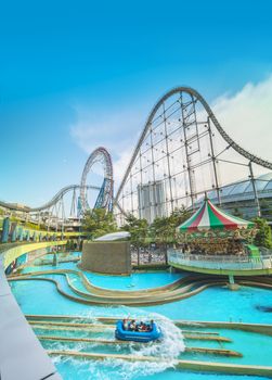 Laqua Tokyo Dome City Mall with its impressive roller coaster integrated in the gallery of its shopping center with a carousel  and water coaster under the summer blue sky.