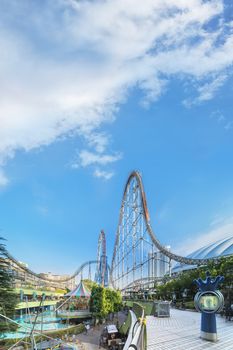 Laqua Tokyo Dome City Mall with its impressive roller coaster integrated in the gallery of its shopping center with a carousel  and water coaster under the summer blue sky.