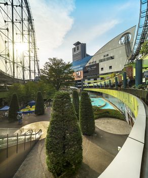 Laqua Tokyo Dome City Mall with its impressive roller coaster integrated into the gallery of its shopping center whose central square is decorated with large firs in the sunset of the summer sky.