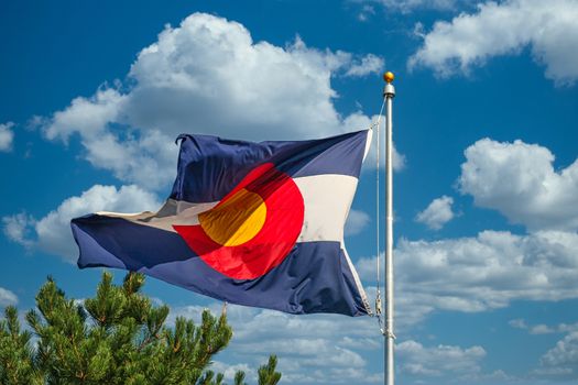 The state flag of Colorado blowing in a breeze under a blue sky