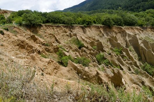 Fragment of the famous Stob’s Pyramids with unusual shape red and yellow rock formations, green bushes and trees around, west share of Rila mountain, Kyustendil region, Bulgaria, Europe