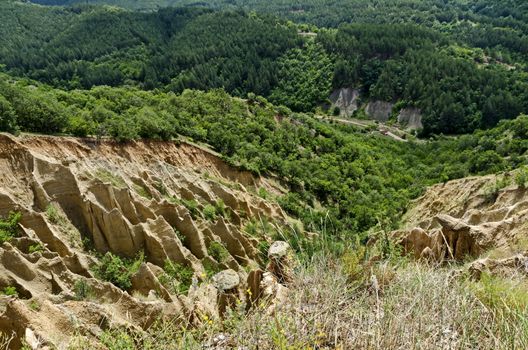 Fragment of the famous Stob’s Pyramids with unusual shape red and yellow rock formations, green bushes and trees around, west share of Rila mountain, Kyustendil region, Bulgaria, Europe