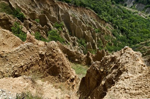 Fragment of the famous Stob’s Pyramids with unusual shape red and yellow rock formations, green bushes and trees around, west share of Rila mountain, Kyustendil region, Bulgaria, Europe