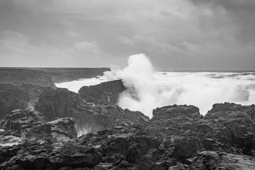 Brimketill lava rock pool Iceland huge wave hitting black basalt coast in black and white