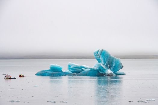 Joekulsarlon Glacier Lagoon deep blue ice with layers of volcanic ash next to motor boats