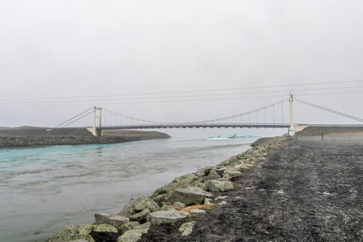 Joekulsarlon Glacier Lagoon channel bridged by suspension bridge washing icebergs towards the Diamond Beach in Iceland