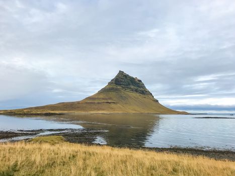 Kirkjufell in Iceland famous mountain reflecting in flat lake during cloudy day
