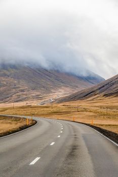 Northern Iceland empty road winding through valley upwards a mountain during unpleasant grey weather
