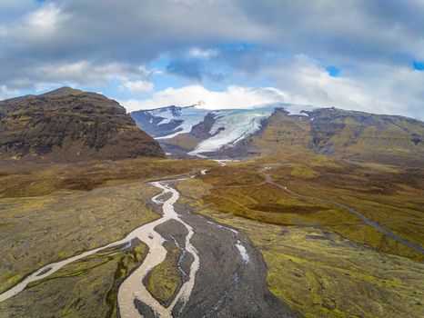 Vatnajoekull glacier in Iceland melting water from glacier forming river and cutting through grass lands