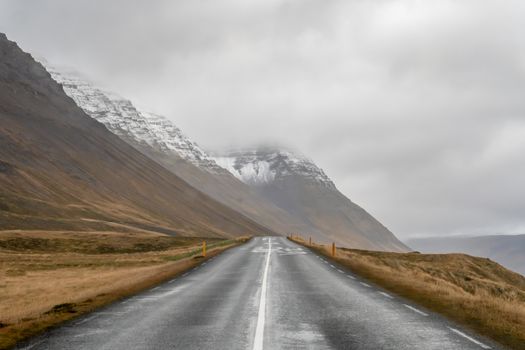 West fjords of Iceland road next to steep mountain slope with snow on top