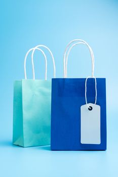 Two blue shopping or gift bags with blank label tag isolated on blue background