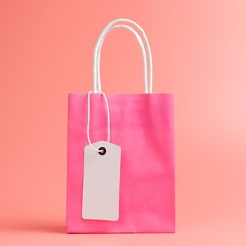One pink shopping or gift bag with blank label tag isolated on pink background