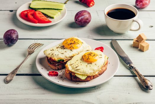 Bruschettas with vegetables and fried egg on white plate, cup of coffee and some fruits over wooden background. Healthy food concept.