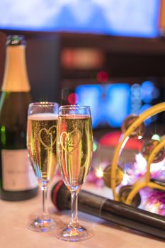 Black microphone in karaoke club, with champagne bottle and couple of sparkling wine glasses, yellow tambourine and screen for singing music on romantic stage party. 