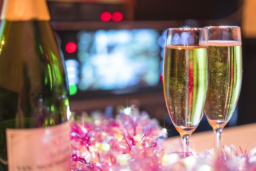 Romantic couple of champagne flutes and bottle of sparkling wine with pink garland decoration for a wedding anniversary party.