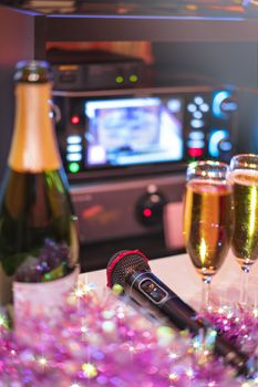 Black microphone in karaoke club, with remote controller, melon and strawberry soda drinks, yellow tambourine and screen for singing music on stage party. 