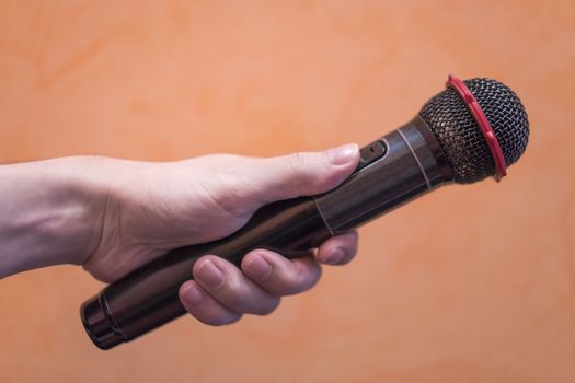 Close-up of a man's hand holding a black microphone on an orange background.