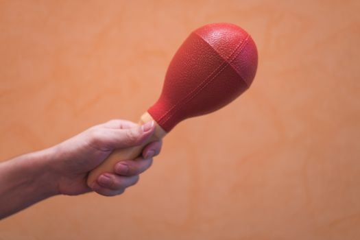 Close-up of a man's hand holding a red maraca on an orange background.