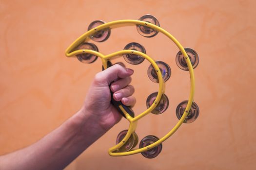 Close-up of a man's hand holding a yellow tambarine on an orange background.