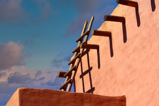 An old wood ladder leaning on a red adobe wall under blue skies