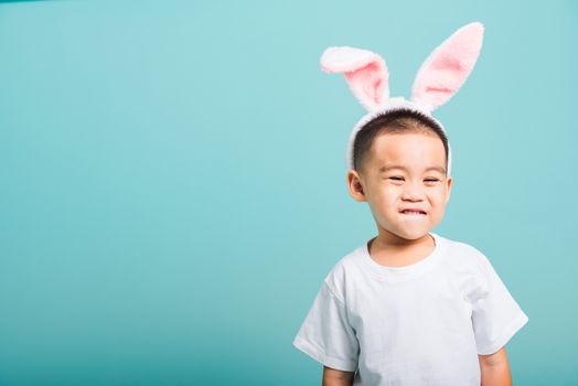 Easter day concept, Happy Asian cute little child boy smile beaming wearing bunny ears and white T-shirt standing on blue background with copy space