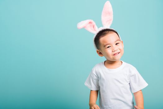 Easter day concept, Happy Asian cute little child boy smile beaming wearing bunny ears and white T-shirt standing on blue background with copy space