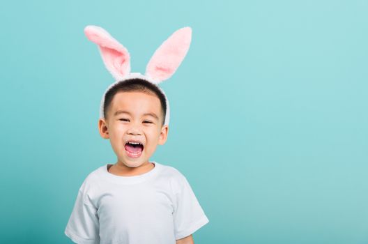 Easter day concept, Happy Asian cute little child boy smile beaming wearing bunny ears and white T-shirt standing on blue background with copy space