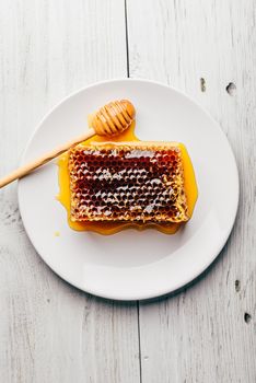 Top view of delicious yummy honeycomb on bright plate with honey dipper over light wooden background