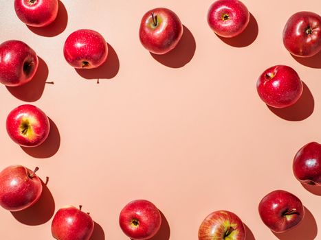 Red apples on orange or coral pink background with copy space for text or design in center. Colorful fruit frame. Creative concept. Flat lay or top view, Hard light