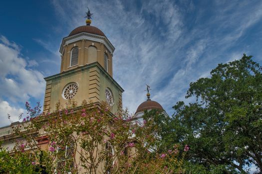 A classic church of brown stucco wtih domes steeples behind trees