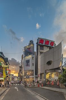 Sunset sky on owl iron mask Shaped of Shibuya Police Station Udagawa Kōban designed by architect Edward Suzuki and opened in April of 1985 in the Inokashira Steet of Shibuya Center Gai which literally means Shibuya Central District. The busiest street once intersected with Shibuya Station, it stretches for 350 meters and incorporates the adjacent streets of Bunkamura, Inokashira and Utagawa into its neighborhood. In 2011 the street was renamed Basketball Street in reference to the holy place of Japanese basketball which is the Yoyogi National Gymnasium to which this street leads. The photo is taken in summer at the Tanabata Star Festival where the portal is adorned with paper decorations in the shape of shooting stars for the occasion.