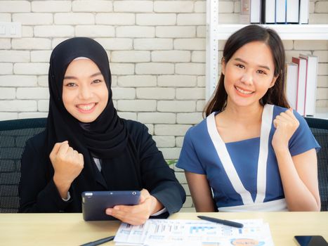 Two Muslim businesswomen are discussing company earnings happily in the modern office.