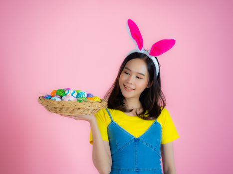 Portrait of a happy young woman wearing Easter bunny ears prepares to celebrate Easter on a pink background.