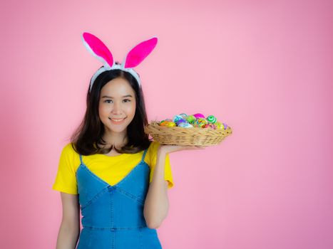 Portrait of a happy young woman wearing Easter bunny ears prepares to celebrate Easter on a pink background.