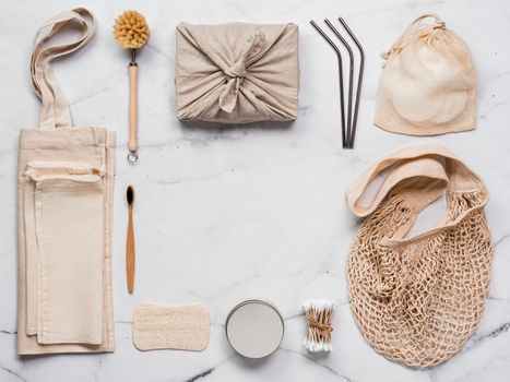 Zero waste concept. Textile wrapping gift, eco bags, metal straws, eco-friendly kitchen tools, bamboo toothbrush and cotton buds, reusable cotton pads on white marble background. Copy space, top view