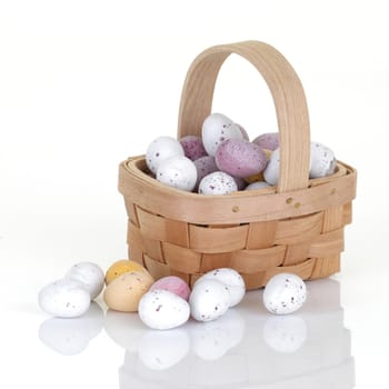 A wood basket of small easter egg candy on white with reflection