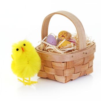 An Easter chick and candy eggs in a basket with straw on white