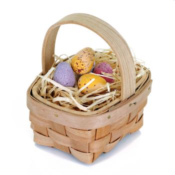 A wicker basket with straw and small easter candy eggs on white