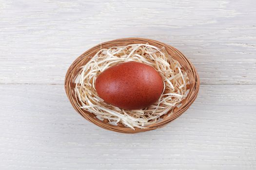 A single brown speckled egg in oval basket with straw on wood background concentric rings