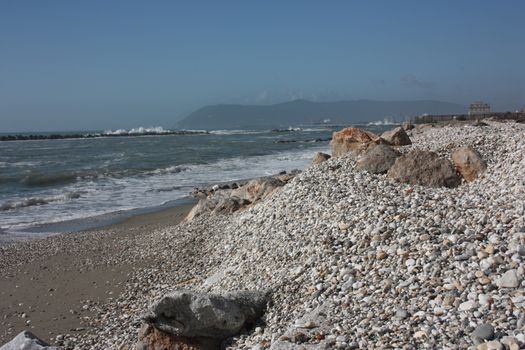 sea ​​with sandy beach and rocks with a view of the fiat tower in massa carrara in tuscany in front of the don gnocchi hospital in italy